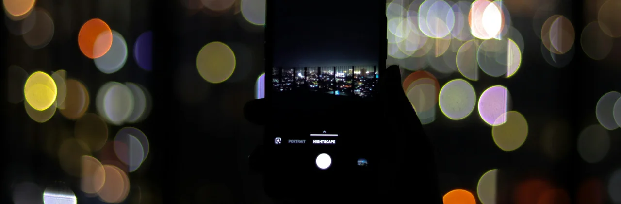 Un celular sostenido de noche frente a luces desenfocadas
