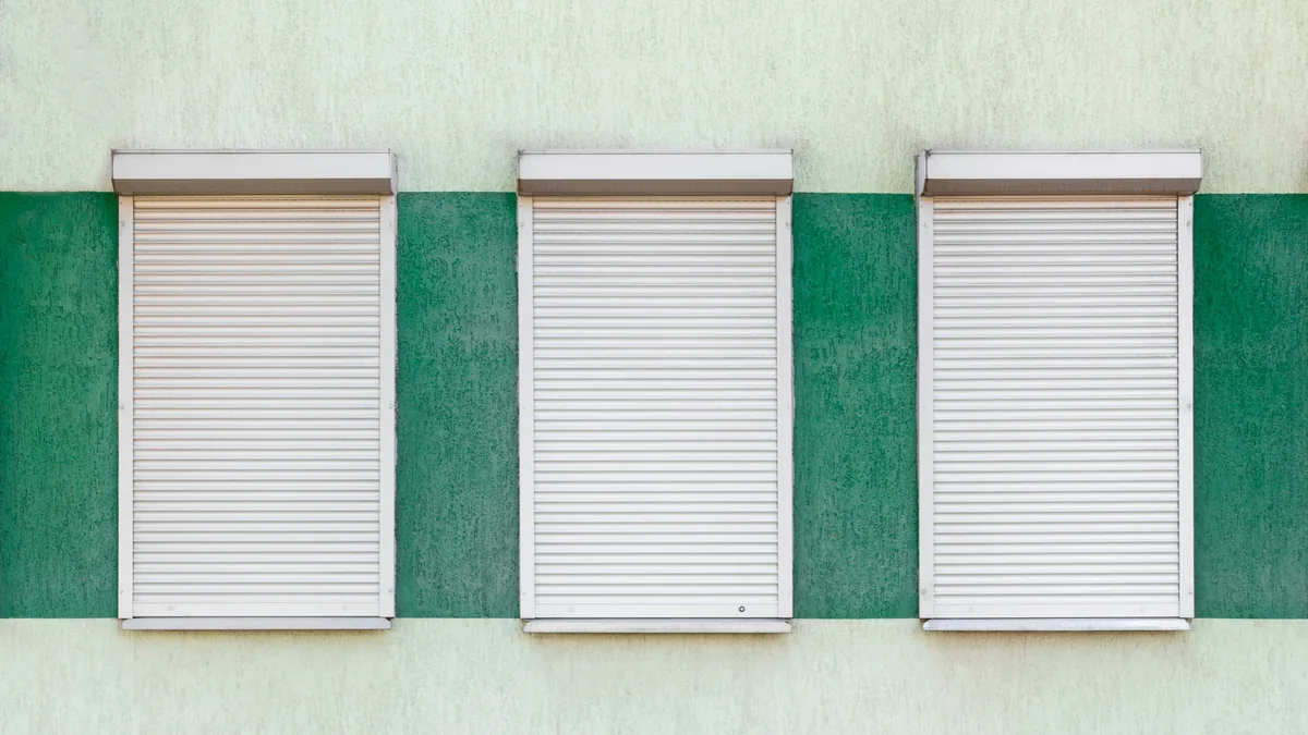 Tres cortinas metálicas blancas cerradas sobre un muro verde