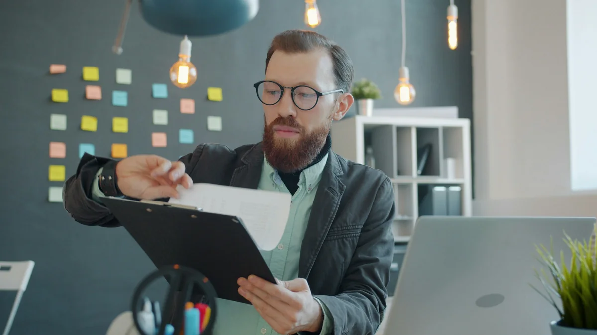 Un hombre con lentes revisando un documento en un escritorio