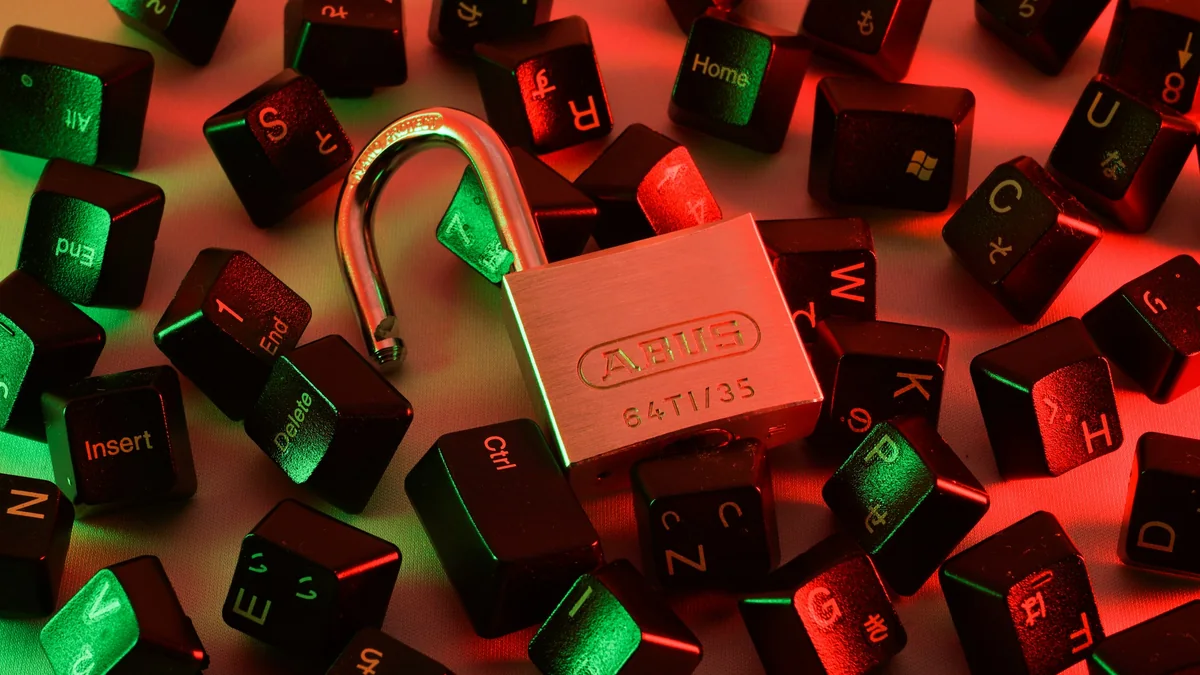 Un candado abierto entre teclas de teclado desperdigadas, bajo luz roja y verde